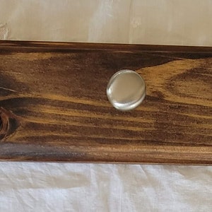 May include: A wooden wall mounted coat rack with five silver hooks. The rack is stained a dark brown color and has a natural wood grain pattern.