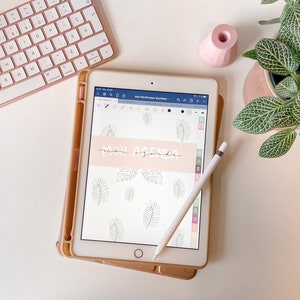 May include: A digital tablet with a white case and a white stylus. The screen displays a digital planner with the text "Mon Agenda" in a handwritten font. The background of the planner is a light pink with a pattern of leaves.