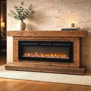 May include: A rustic wooden electric fireplace mantel with a dark brown finish and a black rectangular firebox insert featuring glowing orange flames and faux logs. A white ceramic vase with green eucalyptus branches sits on the mantel.