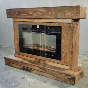 May include: An electric fireplace insert encased in a rustic, dark-stained wooden frame. The unit features a rectangular black glass front with a visible flame effect inside, a thick wooden mantel top, and a sturdy wooden base platform.
