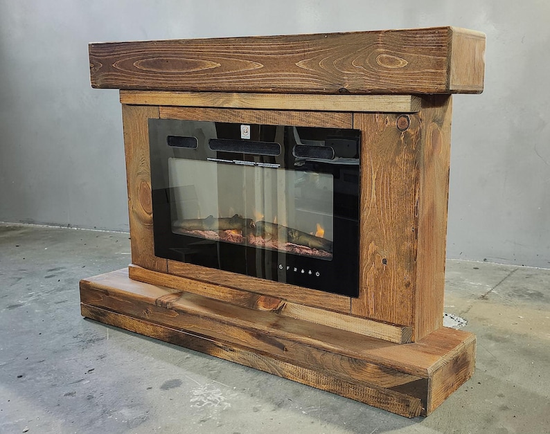 May include: An electric fireplace insert encased in a rustic, dark-stained wooden frame. The unit features a rectangular black glass front with a visible flame effect inside, a thick wooden mantel top, and a sturdy wooden base platform.