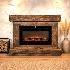 May include: An electric fireplace featuring a dark brown stained wooden mantel and base with a black glass front displaying a simulated orange flame effect over glowing logs, positioned on a light-colored floor with a textured rug in the foreground.