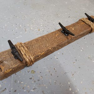 Solid wood nautical theme style look wall mounted coat or towel rack for the bathroom or entryway. This coastal themed towel hooh has rust proof black cast iron boat dock cleats or deck hooks. the wood is distressed and aged with the look of driftwood or reclaimed wood.