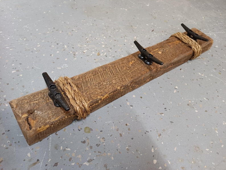 Solid wood nautical theme style look wall mounted coat or towel rack for the bathroom or entryway. This coastal themed towel hooh has rust proof black cast iron boat dock cleats or deck hooks. the wood is distressed and aged with the look of driftwood or reclaimed wood.