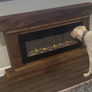May include: A rustic wooden electric fireplace mantel with a dark brown finish and a thick, textured top beam. The unit features a rectangular black glass front displaying a simulated flame effect with glowing orange and yellow light accents.