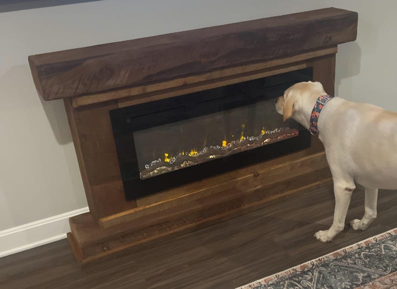 May include: A rustic wooden electric fireplace mantel with a dark brown finish and a thick, textured top beam. The unit features a rectangular black glass front displaying a simulated flame effect with glowing orange and yellow light accents.