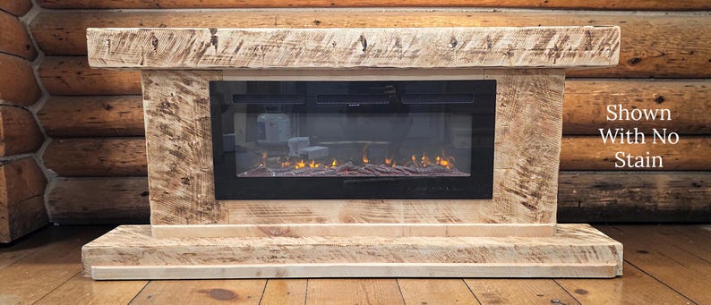 May include: A rectangular electric fireplace with a light-colored, textured natural wood mantel and base. The center features a black glass panel displaying a digital flame effect. Text on the right side reads: Shown With No Stain.