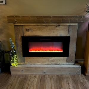 May include: A rectangular electric fireplace insert with a black frame and a simulated glowing orange flame effect, encased in a rustic, light brown wooden mantel surround featuring a thick top shelf and a solid base with visible wood grain.