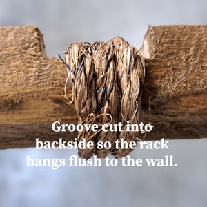 May include: Close-up of a wooden rack with a woven, natural fiber rope detail. The text on the image reads: "Groove cut into backside so the rack hangs flush to the wall."