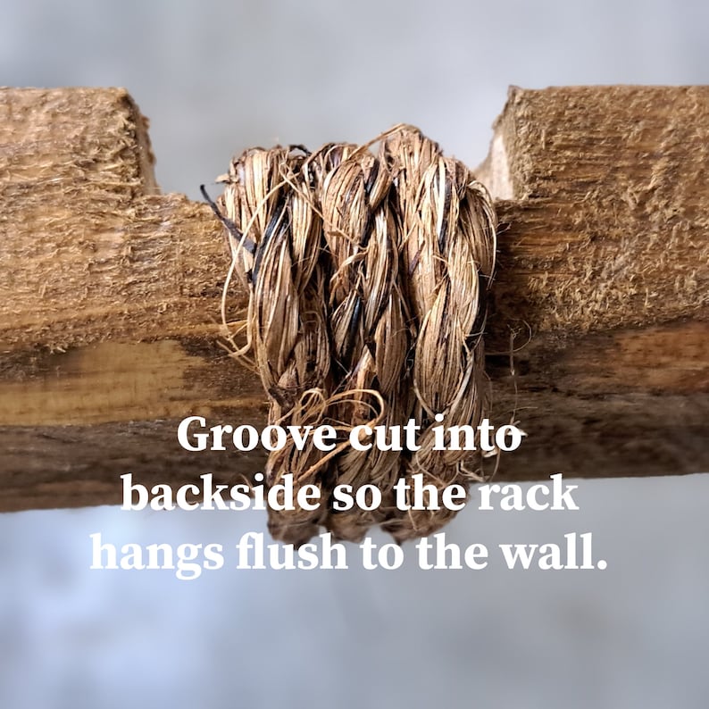 May include: Close-up of a wooden rack with a woven, natural fiber rope detail. The text on the image reads: "Groove cut into backside so the rack hangs flush to the wall."