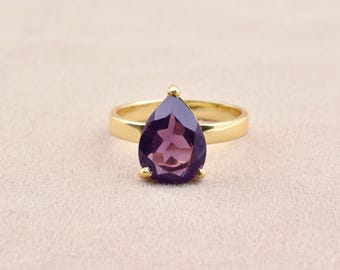 May include: A gold ring with a pear-shaped purple gemstone.