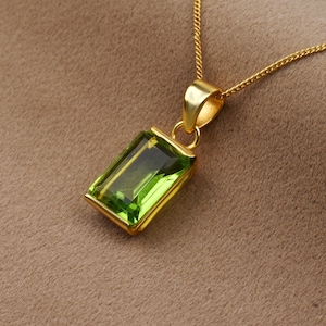May include: A gold chain necklace with a pendant featuring a large, rectangular, emerald green gemstone.