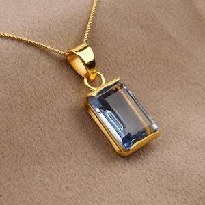 Könnte beinhalten: Eine goldene Kettenkette mit einem Anhänger, der einen rechteckigen, hellblauen Edelstein zeigt.