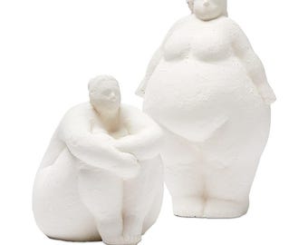 May include: Two white ceramic sculptures of people. One is standing with their arms at their sides, and the other is sitting with their arms crossed.