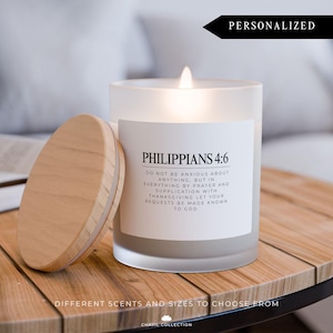 May include: A white frosted glass candle with a wooden lid. The candle has a quote from Philippians 4:6 printed on the front. The candle is sitting on a wooden table. The text reads: "Do not be anxious about anything, but in everything by prayer and supplication with thanksgiving let your requests be made known to God."