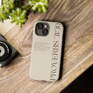Puede incluir: Una funda de smartphone beige con el texto PROVERBS 31:30 en letras verticales grandes y el vers&iacute;culo Charm is deceptive, and beauty is fleeting; but a woman who fears the Lord is to be praised en fuente m&aacute;s peque&ntilde;a a la izquierda.