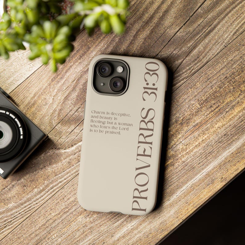 Puede incluir: Una funda de smartphone beige con el texto PROVERBS 31:30 en letras verticales grandes y el vers&iacute;culo Charm is deceptive, and beauty is fleeting; but a woman who fears the Lord is to be praised en fuente m&aacute;s peque&ntilde;a a la izquierda.