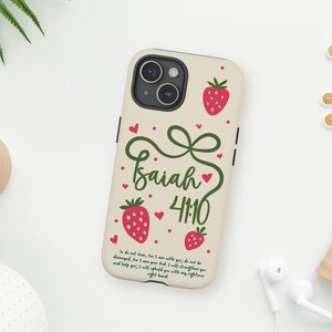 May include: A beige phone case with red strawberry illustrations and the text "Isaiah 41:10" in green script. The case has a bow design and a Bible verse. The phone case is on a white surface.