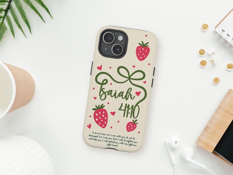 May include: A beige phone case with red strawberry illustrations and the text "Isaiah 41:10" in green script. The case has a bow design and a Bible verse. The phone case is on a white surface.