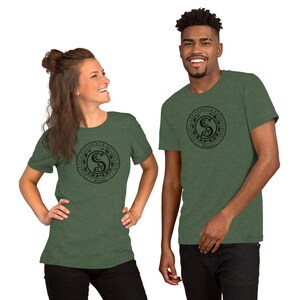 May include: Two people wearing green heather t-shirts with a black and white graphic of a circle with a stylized "S" inside. The circle has the text "Society of Florists &  Adjacent Interests" around the outside and "Mystic" at the bottom.