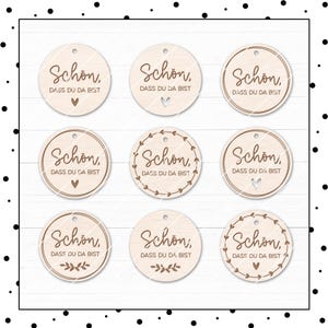 May include: Nine round wooden tags with the text "Schon, Dass du da bist" in brown lettering. Some tags have a heart design, while others have a wreath design.