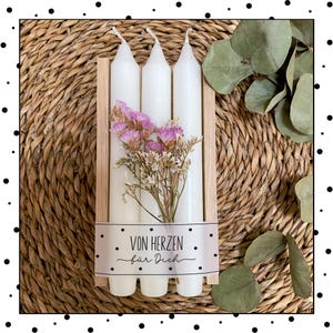 May include: Three white candles in a wooden box with a label that says "Von Herzen f&uuml;r Dich". The candles are surrounded by dried flowers.