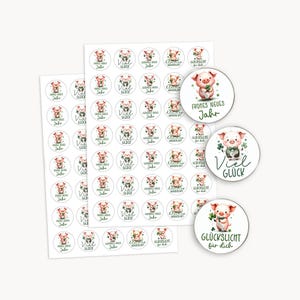 Puede incluir: Hojas de pegatinas con ilustraciones de acuarela de cerdos sosteniendo tréboles. Las pegatinas tienen texto en alemán, incluyendo "Frohes Neues Jahr" y "Viel Glück". Algunas pegatinas son redondas, otras rectangulares.