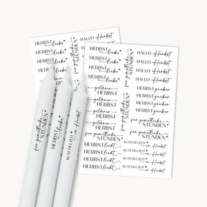 Könnte beinhalten: Drei weiße Stabkerzen mit schwarzer Schrift, neben Aufkleberbögen. Der Text enthält "HERBST liebe" und "KUSCHELZEIT in Herbst". Die Aufkleber zeigen verschiedene Schriftarten und Phrasen.