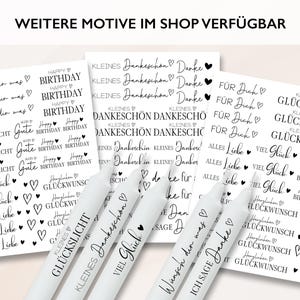 Puede incluir: Un conjunto de velas blancas y tarjetas con texto negro. Las tarjetas presentan frases como "Feliz Cumplea&ntilde;os", "Gracias" y "Buena Suerte", junto con ilustraciones de corazones. El texto "WEITERE MOTIVE IM SHOP VERF&Uuml;GBAR" est&aacute; en la parte superior.