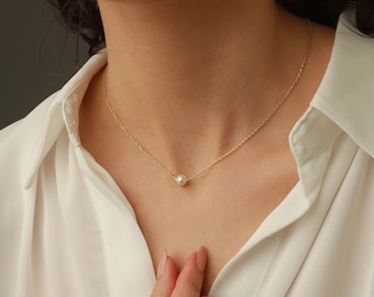 May include: A delicate gold chain necklace featuring a single, centered, round white pearl. The necklace rests against the collarbone, showcasing a minimalist design with a thin, polished metal link chain and a smooth, lustrous pearl pendant.