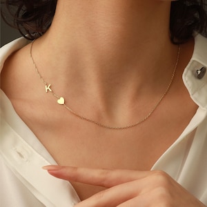 Könnte beinhalten: Eine goldene Kettenkette mit einem kleinen Herz-Anhänger und einem Buchstaben 'K'-Anhänger.