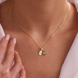 May include: A gold-toned chain necklace featuring two small, rectangular, vertical pendant tags. Each tag is engraved with a single letter, specifically the characters R and S, suspended from the delicate link chain by small circular jump rings.