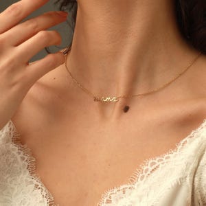 May include: A gold-toned necklace featuring a delicate chain and a central pendant in cursive script that spells out the word mama. The metal has a polished finish, and the script lettering is integrated directly into the chain structure.