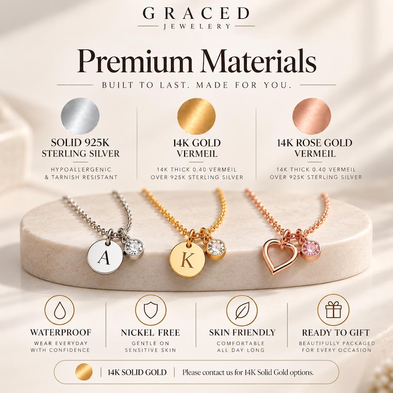 May include: Three necklaces displayed on a stone base: a silver necklace with an A charm and crystal, a gold necklace with a K charm and crystal, and a rose gold necklace with a heart charm and crystal. Text includes Premium Materials and features.