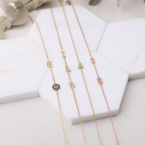 May include: Four gold necklaces with different charms. The charms include the letters E, Z, A, and S. One necklace has a blue evil eye charm.