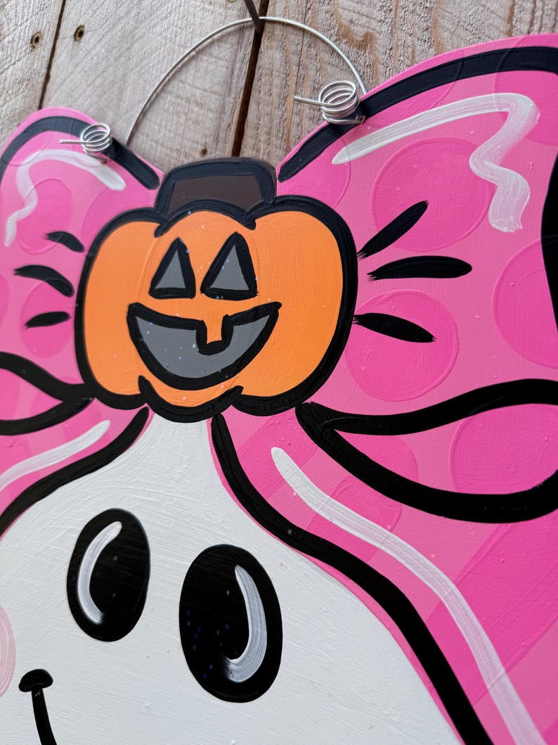 May include: A pink and white ghost with a black outline and a pumpkin on its head. The pumpkin has a black outline and a smiling face with triangle eyes. The ghost has black eyes and a black mouth.