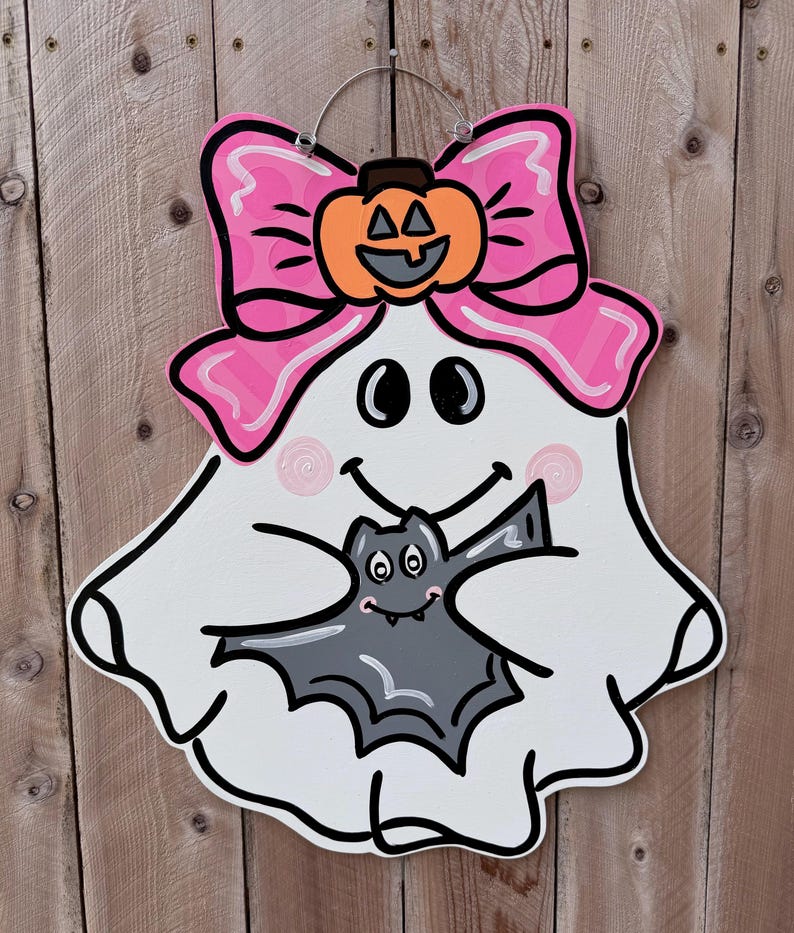 May include: A white ghost with a pink bow and a pumpkin on its head is holding a gray bat. The ghost is smiling and has two pink swirls on its cheeks.