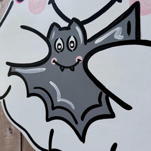 May include: A white ghost with a pink bow and a black outline holds a gray bat with white eyes and a black mouth. The bat has a pink blush on its cheeks.
