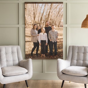 May include: A family portrait featuring a group of five people standing in a wooded area. The family are dressed in casual clothing and smiling. The photo is printed on a canvas and framed with a wooden frame.