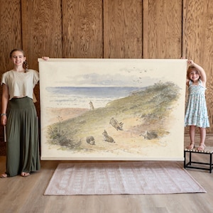 May include: A vintage-style illustration of a beach scene with a group of rabbits running on the sand. The illustration is printed on a canvas and is being held up by two people.