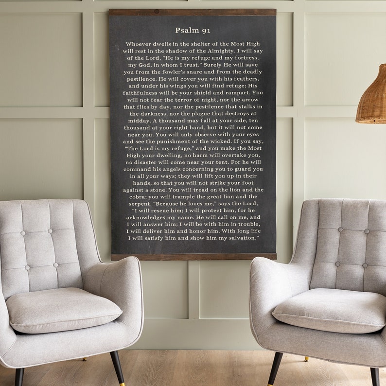 May include: A black framed chalkboard sign with white text that reads "Psalm 91" and includes a passage from the Bible about finding refuge in God. The sign is hanging on a wall with two gray chairs in front of it.