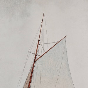 May include: A close-up of a sailboat's mast and sail. The sail is white and the mast is brown. The sky is a light gray.