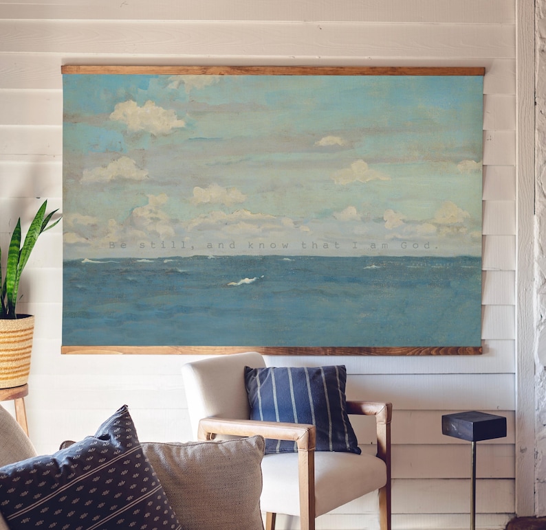 Pu&ograve; includere: Un'opera d'arte murale su tela incorniciata raffigurante un paesaggio marino con un oceano blu e un cielo nuvoloso. L'opera d'arte &egrave; incorniciata con un bordo in legno e include il testo "Be still, and know that I am God."