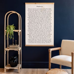 May include: A framed print of Psalm 91, a passage from the Bible, with a wooden frame and a white background. The text is in black font and reads, "Whoever dwells in the shelter of the Most High..."