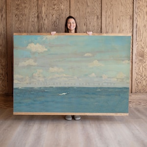 Pu&ograve; includere: Dipinto di paesaggio incorniciato raffigurante una serena scena oceanica sotto un cielo nuvoloso. L'opera presenta sfumature di blu e bianco, con il testo "Be still, and know that I am God." La cornice &egrave; in legno chiaro.