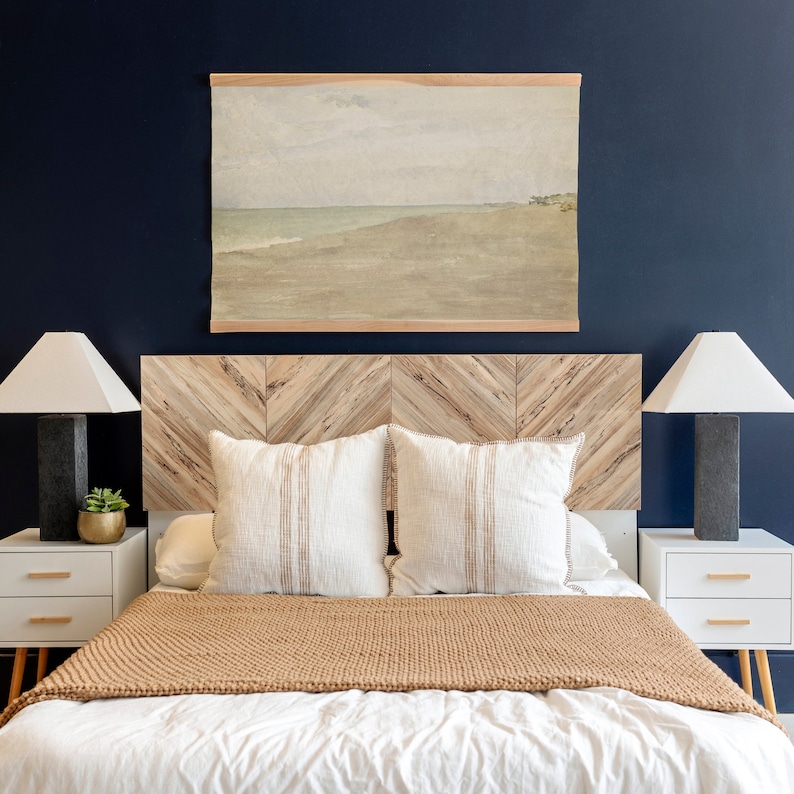 May include: A brown wooden headboard with a chevron pattern, a white bed with a brown throw blanket and two white pillows, and two white lamps with black bases on bedside tables.