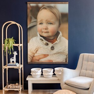 May include: A framed photograph of a young child wearing a white sweater against a brown background. The child is looking at the camera with a serious expression.