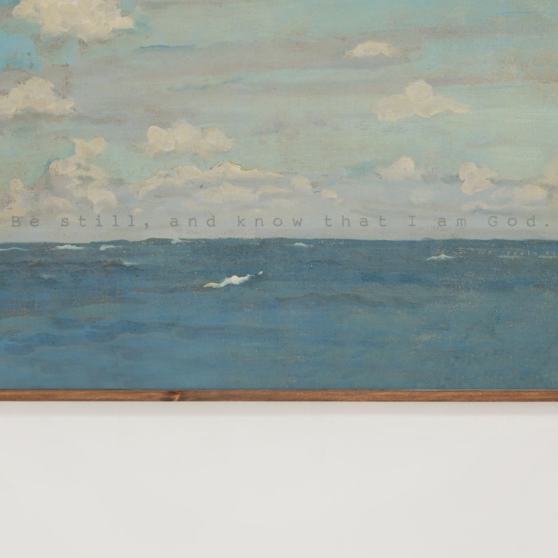 Pu&ograve; includere: Un'opera d'arte incorniciata raffigurante un sereno paesaggio marino con un cielo nuvoloso. L'oceano &egrave; dipinto in tonalit&agrave; di blu, con nuvole bianche e il testo "Be still, and know that I am God." L'opera &egrave; incorniciata in una cornice di legno marrone.