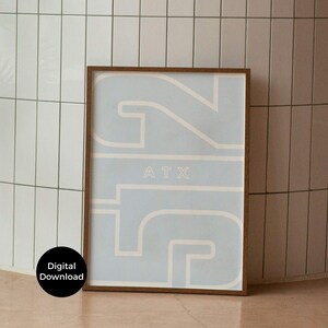 May include: A framed art print featuring a light blue background with a large, stylized number 512 in a lighter beige color. The letters "ATX" are centered within the design. The frame is a dark brown color. A digital download is available.