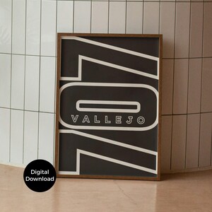 Op de afbeelding: Een ingelijste kunstprint met een donkerbruine houten lijst. Het kunstwerk heeft een zwarte achtergrond met witte geometrische vormen en het woord "VALLEJO" in het wit. Een digitale downloadsticker staat linksonder.